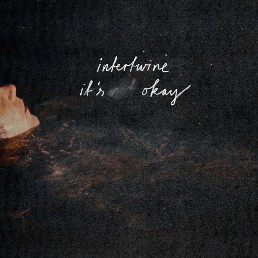 Release-Cover „It's ____ Okay“ von Intertwine: Person schwimmt im Wasser, dass sehr dunkel aussieht, nur der Kopf ist über der Wasserobefläche, das Gesicht ist kurz über der Nase abgeschnitten und nicht erkennbar